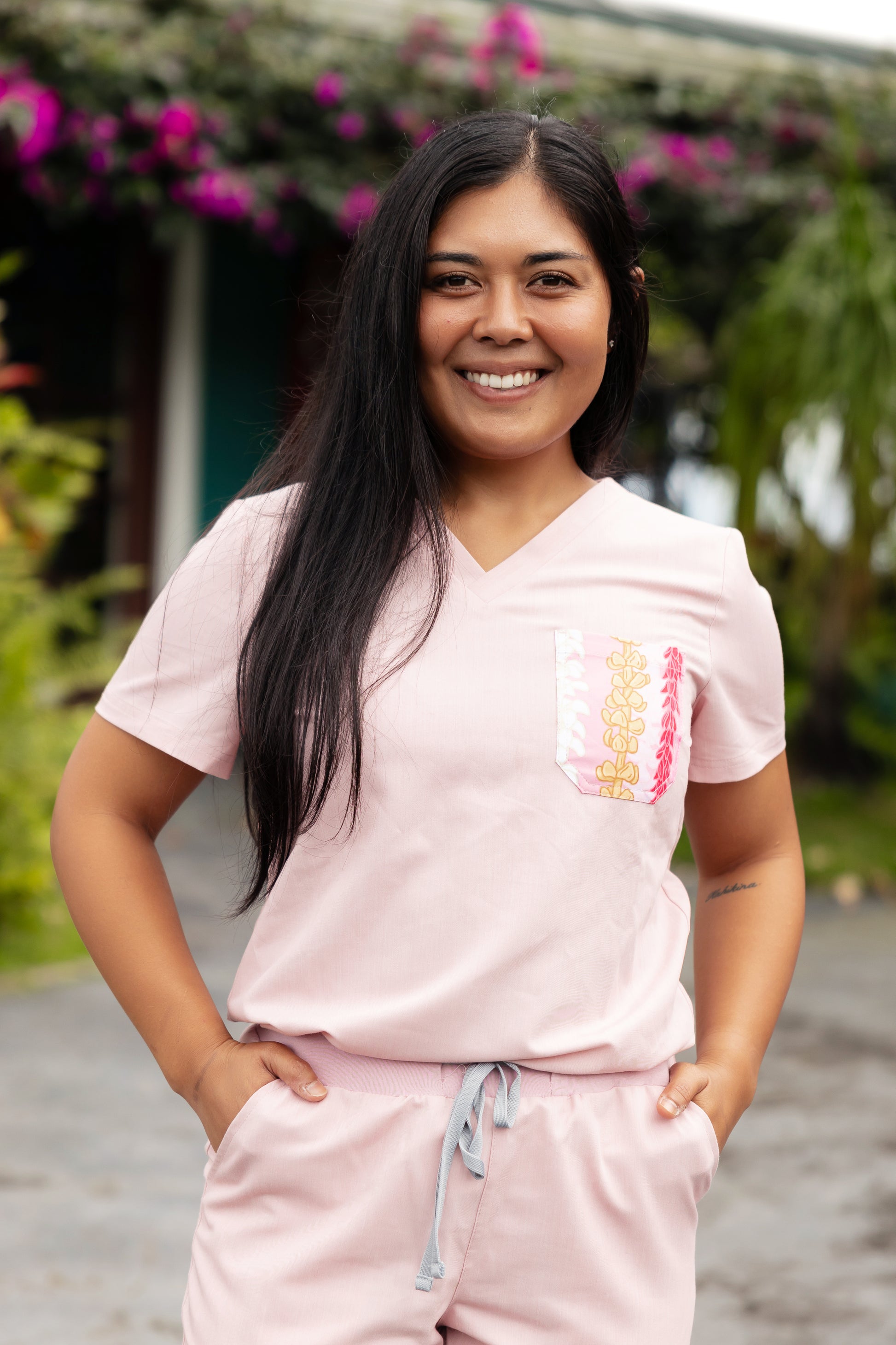 Woman wearing a pink outfit with a colorful Hawaii inspired pocket design, standing outdoors with greenery in the background.