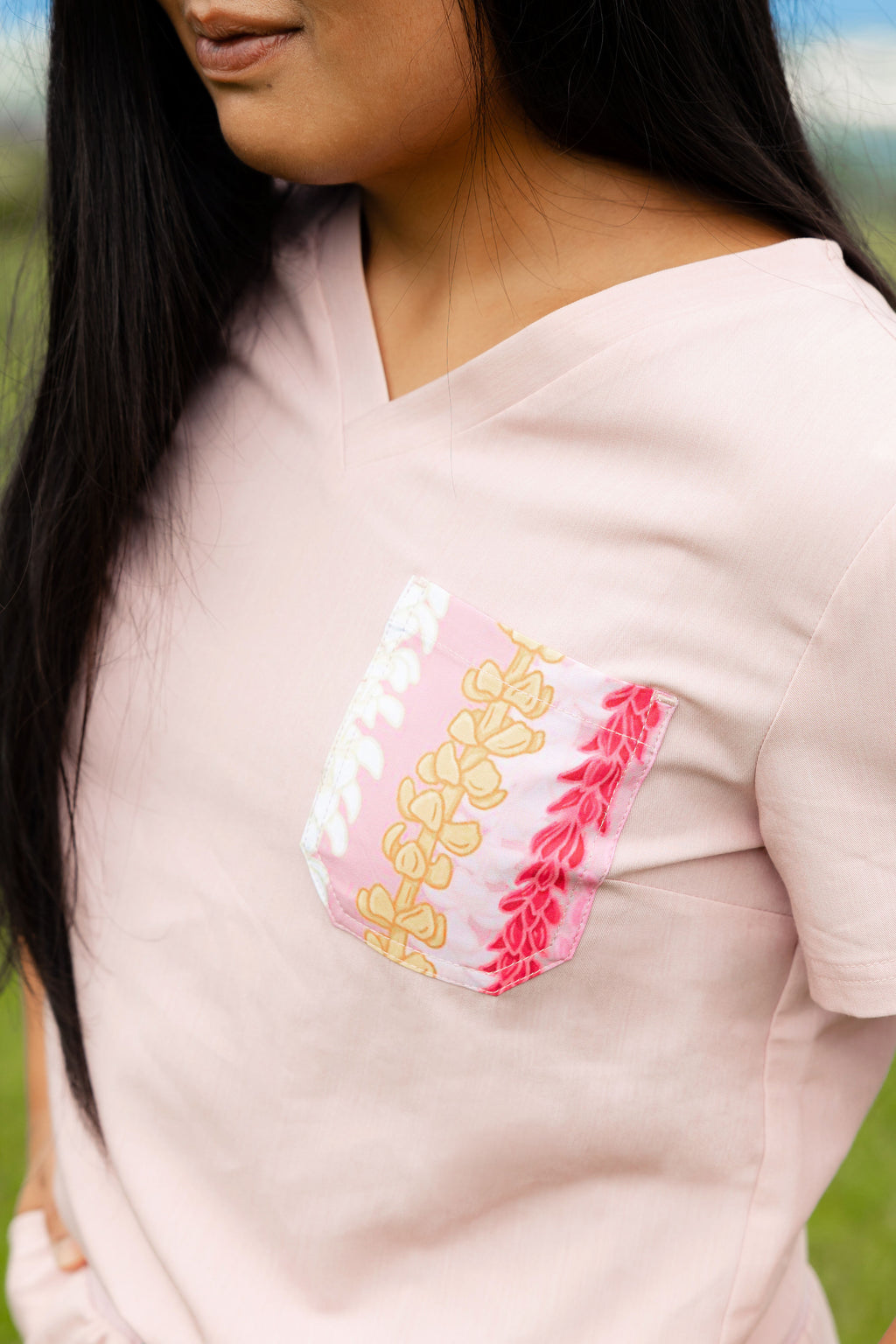Close-up of a light pink scrub top with decorative patch pocket featuring pink Hawaii-inspired floral designs.
