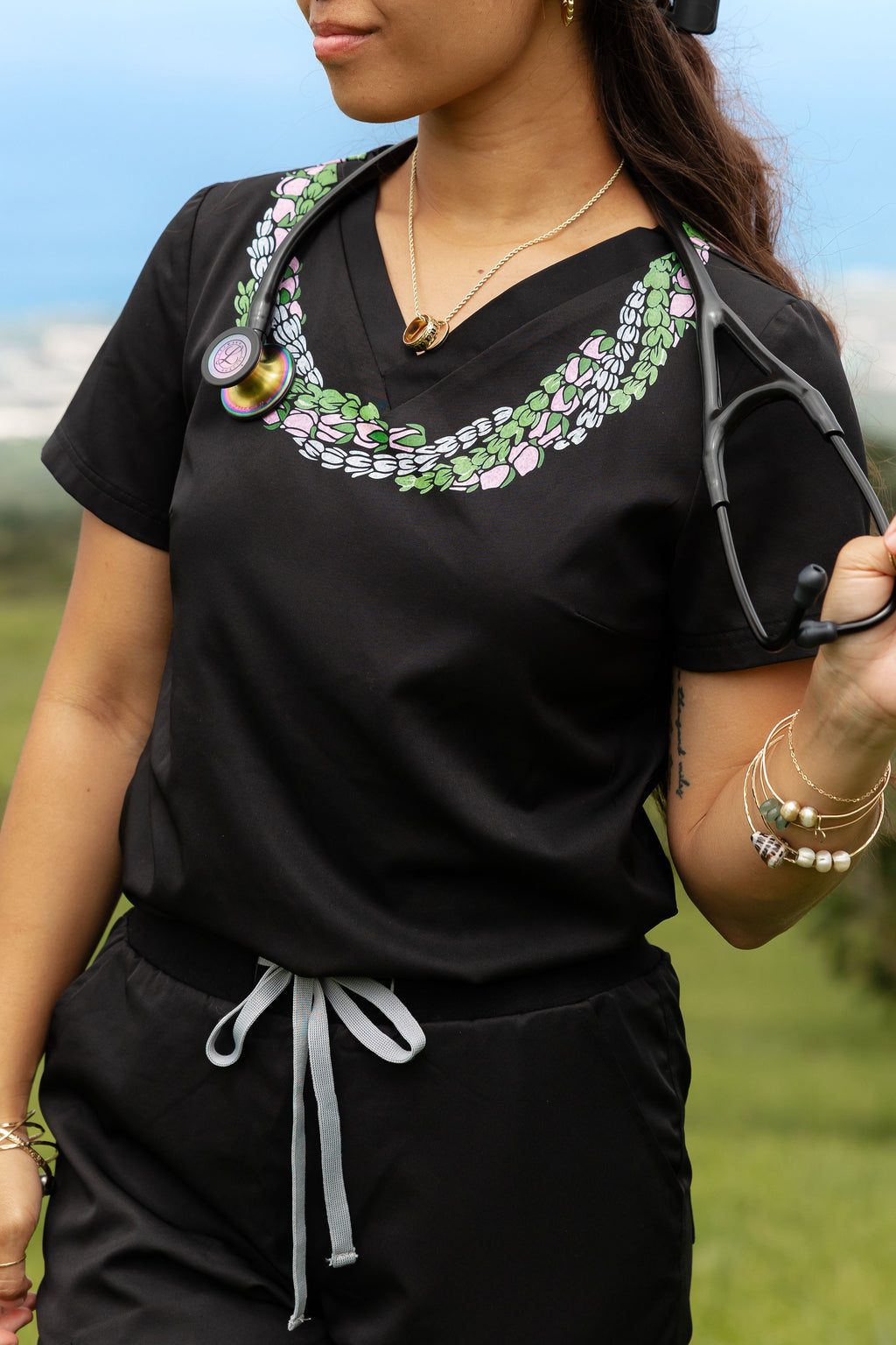 Woman wearing medical scrub top with Hawaii inspired lei design and holding a stethescope